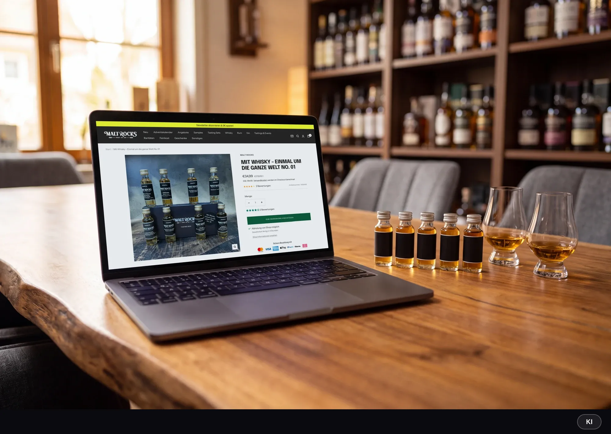KI-generiertes Bild: Laptop auf einem Holztisch im Tasting-Raum zeigt die Malt-Rocks-Produktseite eines Whisky-Tasting-Sets, daneben Sample-Fläschchen und zwei Nosing-Gläser